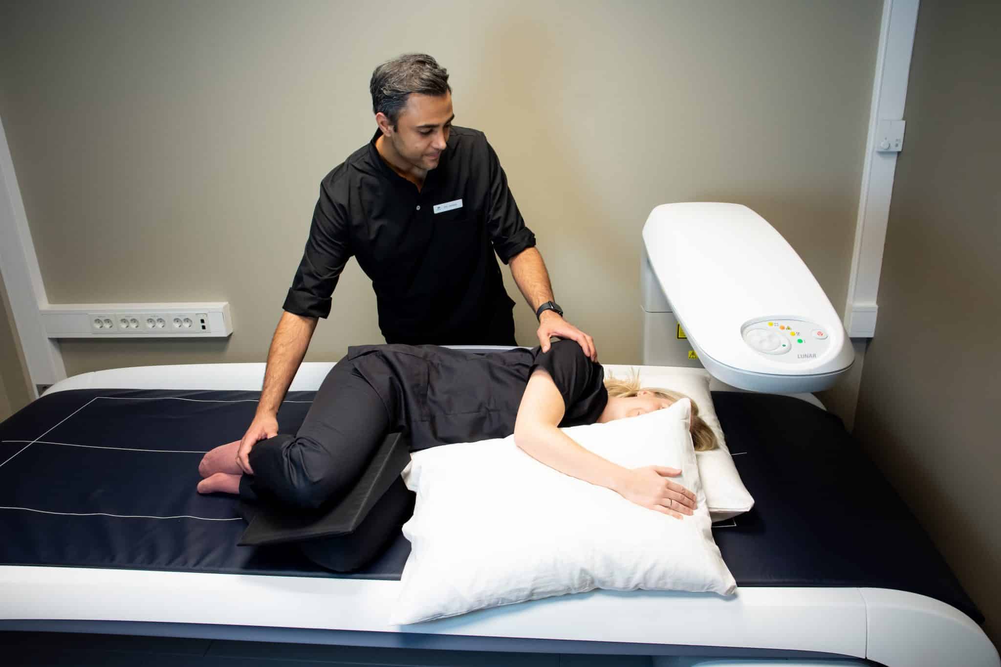 Lege justerer pasient til å ligge i riktig posisjon for en DEXA-scan