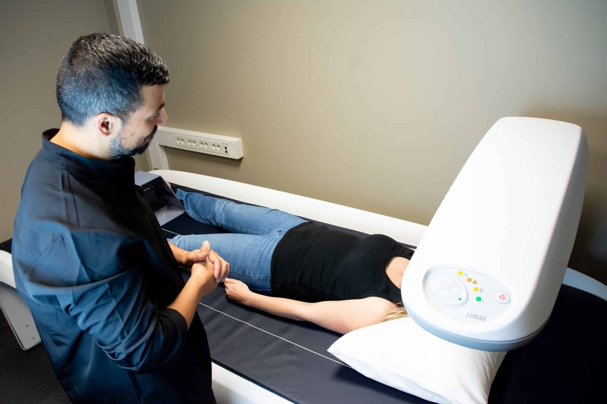 DEXA-scan undersøkelse, lege står og ser på mens DEXA-maskinen scanner kroppen til en pasient