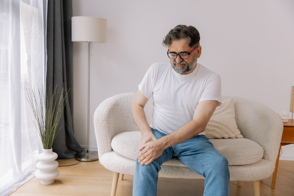 Mann som holder seg på kneet, har vondt i kneet, han har osteoporose