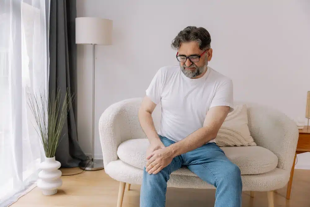 Mann som holder seg på kneet, har vondt i kneet, han har osteoporose